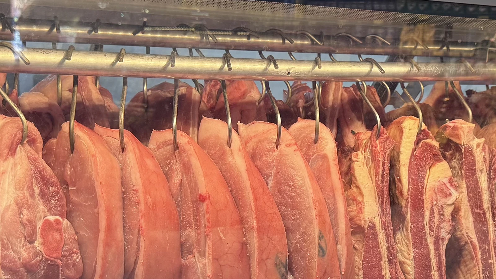Cortes de carne suína e bovina expostos em ganchos no balcão do açougue do Megamix